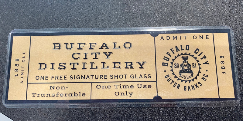 A tan laminated ticket with the words &quot;Buffalo City Distillery One Free Signature Shot Glass.&quot;