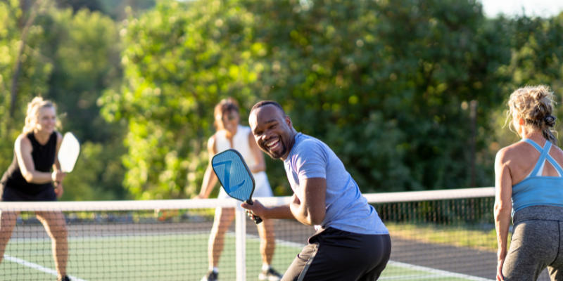 Four people playing pickleball with one laughing and facing the camera.