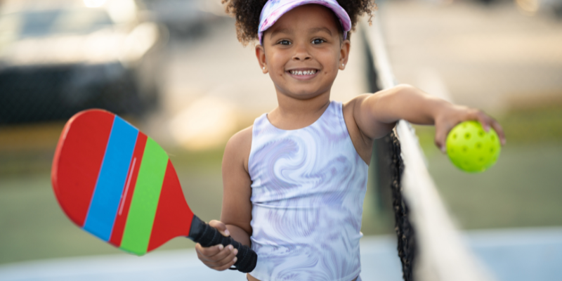 Young girl holding a pickleball racket and pickleball.