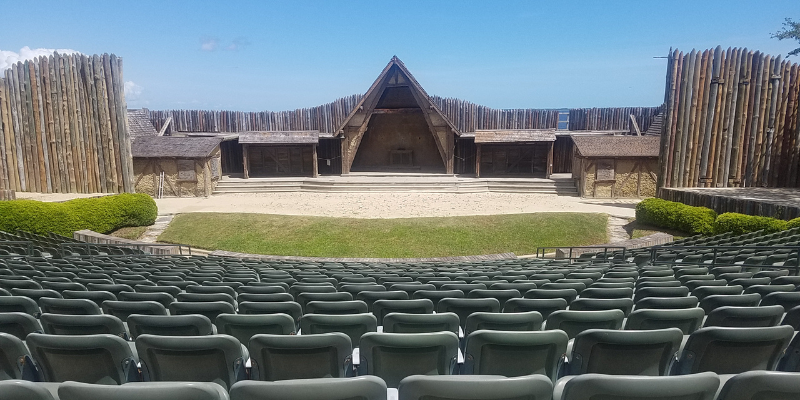 Image shows an outdoor theater with circular seating. The center is a triangle fort with sand and grass in front.